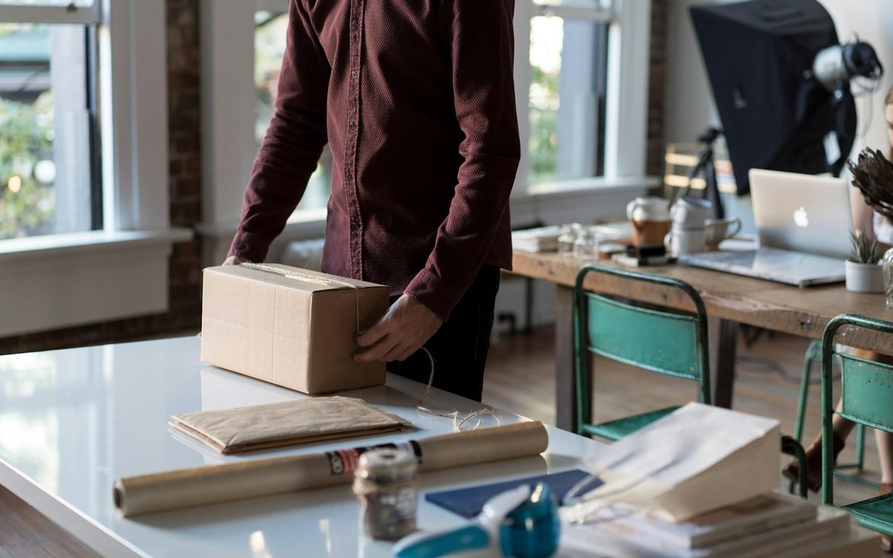 Mann verpackt im Büro einen Karton, im Hintergrund ein MacBook auf dem Schreibtisch