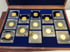 12 goldene Münzen in quadratischen, verspiegelten Haltern auf blauem Samt in einer Holzkiste.