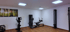 Ein moderner Fitnessraum mit Ergometer, Kraftstation und Seilzug vor weißen Wänden mit einem Waldbild und Holzfußboden.