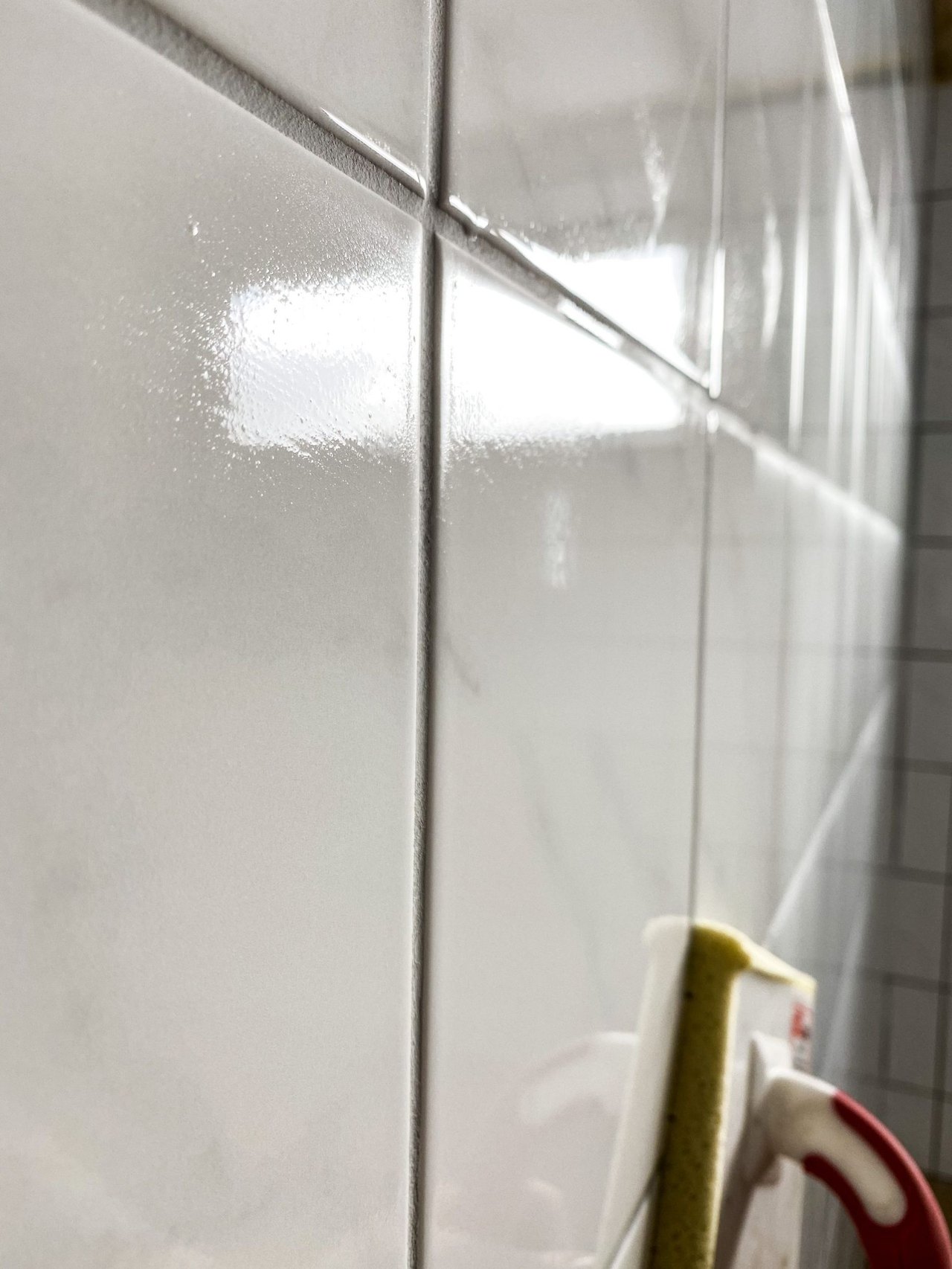 Weiße, glänzende Wandfliesen mit dunklen Fugen und einem Fugenschwamm im Vordergrund.
