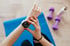 Eine Person mit rotem Nagellack blickt auf eine Smartwatch am Handgelenk über einer blauen Yogamatte, Hanteln im Hintergrund.