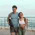 Happy couple in athletic wear with a yoga mat and water bottle, walking by the ocean.