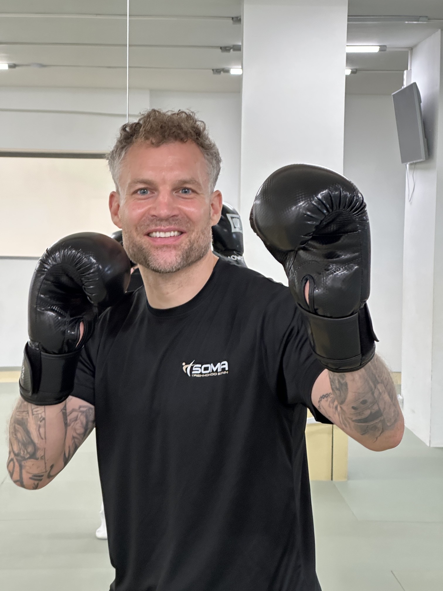 Trainer Carlo im SOMA-Shirt mit Boxhandschuhen im Trainingsraum in Bonn
