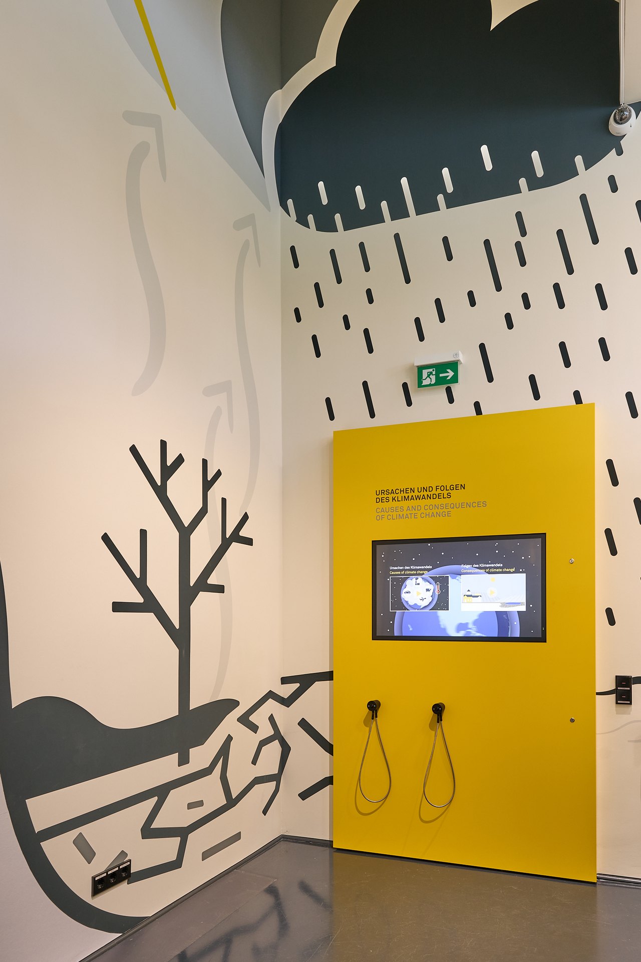 Die Touch-Station ‚Ursachen und Folgen des Klimawandels’, eingebettet in eine großflächige Wandillustration aus Dürre und Starkregen