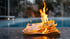 Bündel brennender 50-Euro-Scheine vor einem Pool in der Dämmerung, Flammen schlagen hoch.