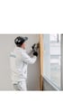 Ein Handwerker in weißer Arbeitskleidung und Kappe versiegelt eine Fensterfuge mit einer Kartuschenpresse.