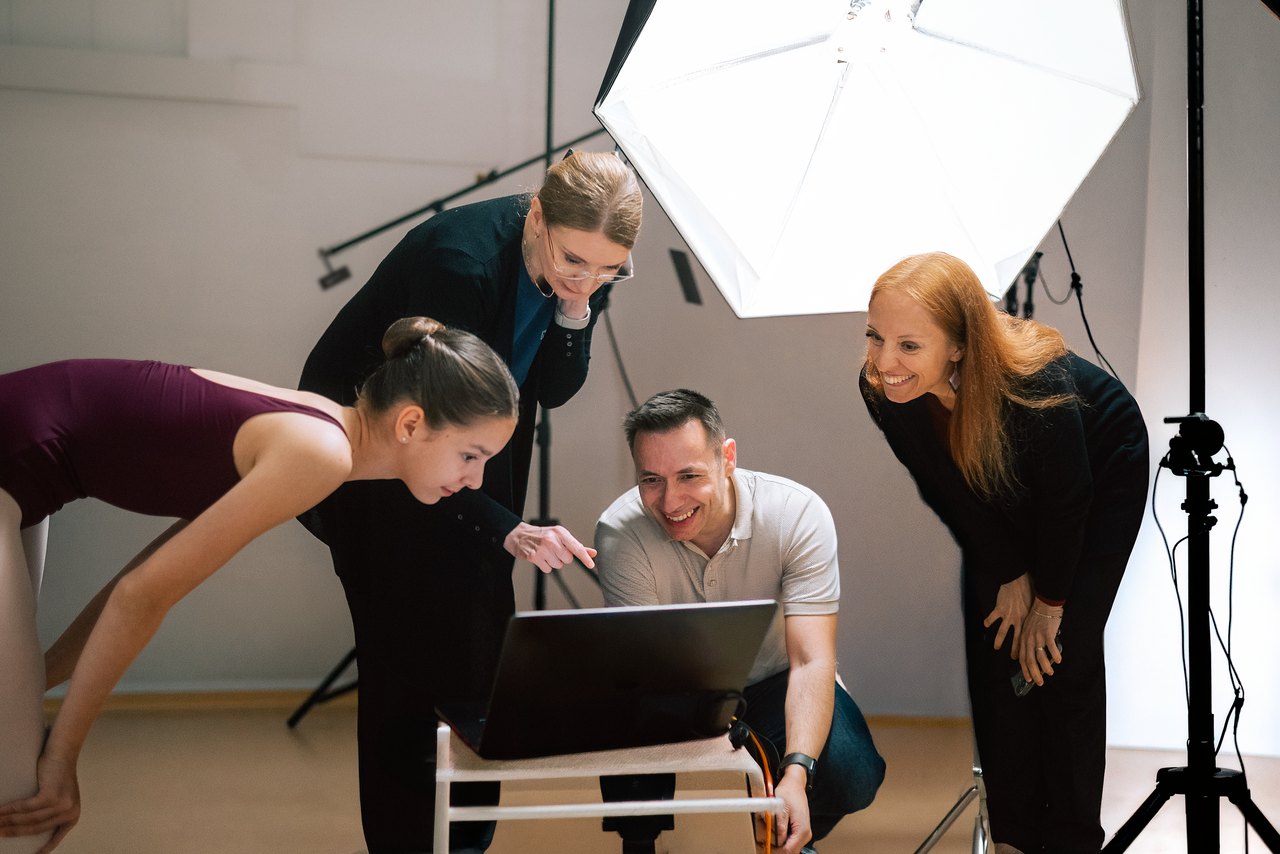 Eine Tänzerin, zwei Coaches und der Fotograf, die sich gemeinsam im Studio Bilder auf einem Laptop ansehen.