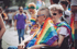 Ein Mann im Rollstuhl mit einer Regenbogenflagge um die Schultern sitzt neben einer Frau mit Sonnenbrille.