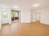Leeres Wohnzimmer mit Holzboden, weißen Wänden und Zugang zu einem Balkon.