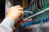 Hände prüfen bunte Elektrokabel mit einem Multimeter in einem Serverraum.