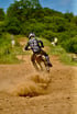 Motocross-Fahrer mit Helm und Trikot „LIGNEY 247“ fährt auf einer staubigen Strecke, Schlamm spritzt vom Hinterrad.