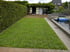 Ein gepflegter Garten mit frisch verlegten Rasengittern, einer hohen Hecke, Gartenhaus und einem angrenzenden Wasserbecken.