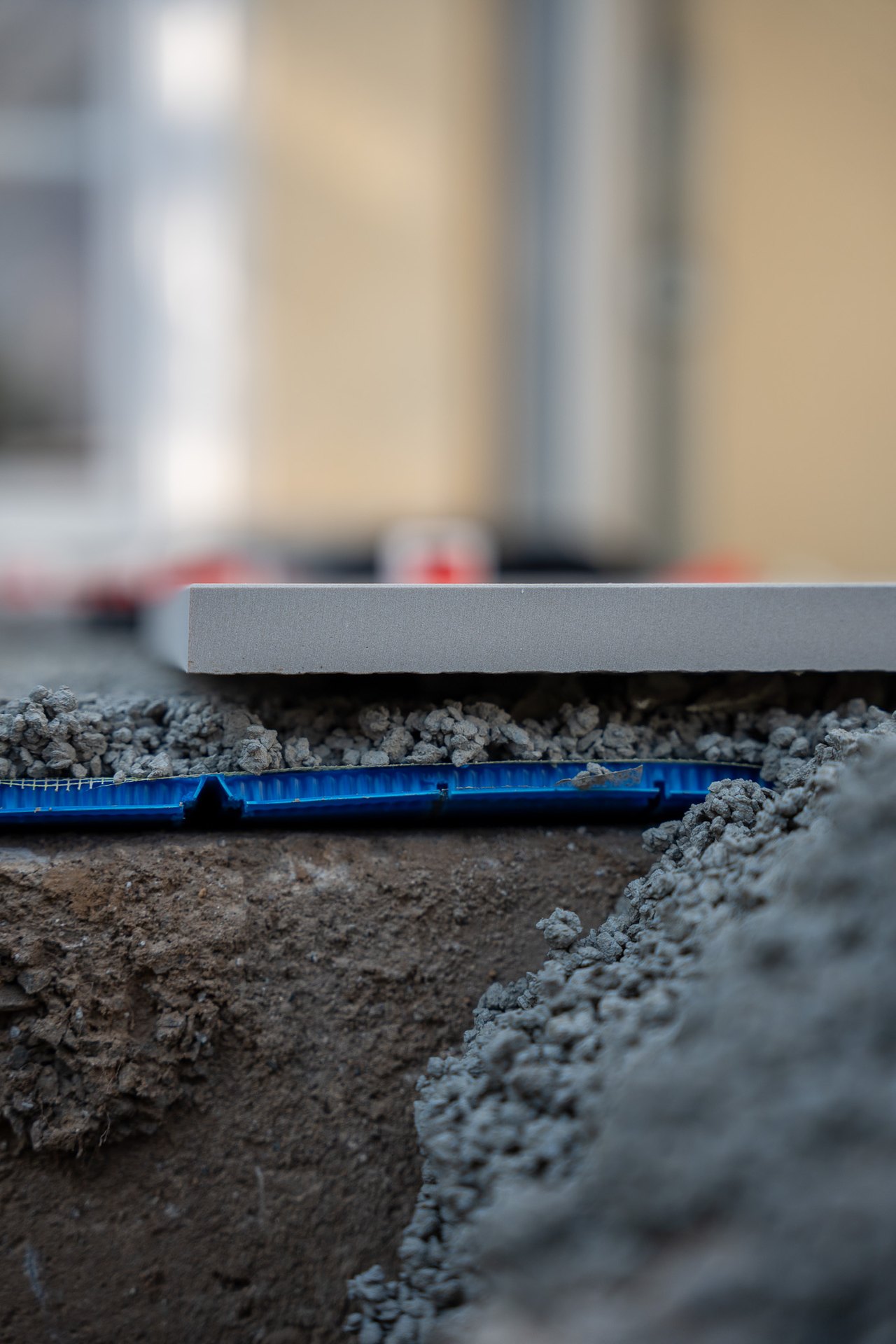Blaue Drainageleitung im Schotterbett unter einer grauen Steinplatte während der Bauphase