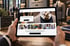 Hände halten ein Tablet mit dem Onlineshop „Gentleman“ in einer Herrenmode-Boutique mit Anzügen im Hintergrund.