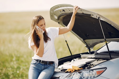 Driver calling a towing service in Corona, CA beside a car with its hood open