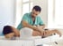 Chiropractor adjusting a male patient's neck and upper back on an examination table.