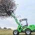 Grüner Avant 750 Kompaktlader mit Baumschere hebt einen Baumstamm mit braunen Blättern in einem Feld.