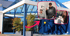 Modernes Firmengebäudeder Teleteam GmbH aus Oldenbburg  mit blauer Glasfassade, ergänzt durch hervorgehobene Bilder von Mitarbeitenden, die im Büro arbeiten und freundlich in die Kamera lächeln.
