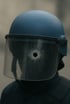 Ein Polizist mit blauem Helm und zerbrochenem Visier mit Einschussloch in der Mitte.