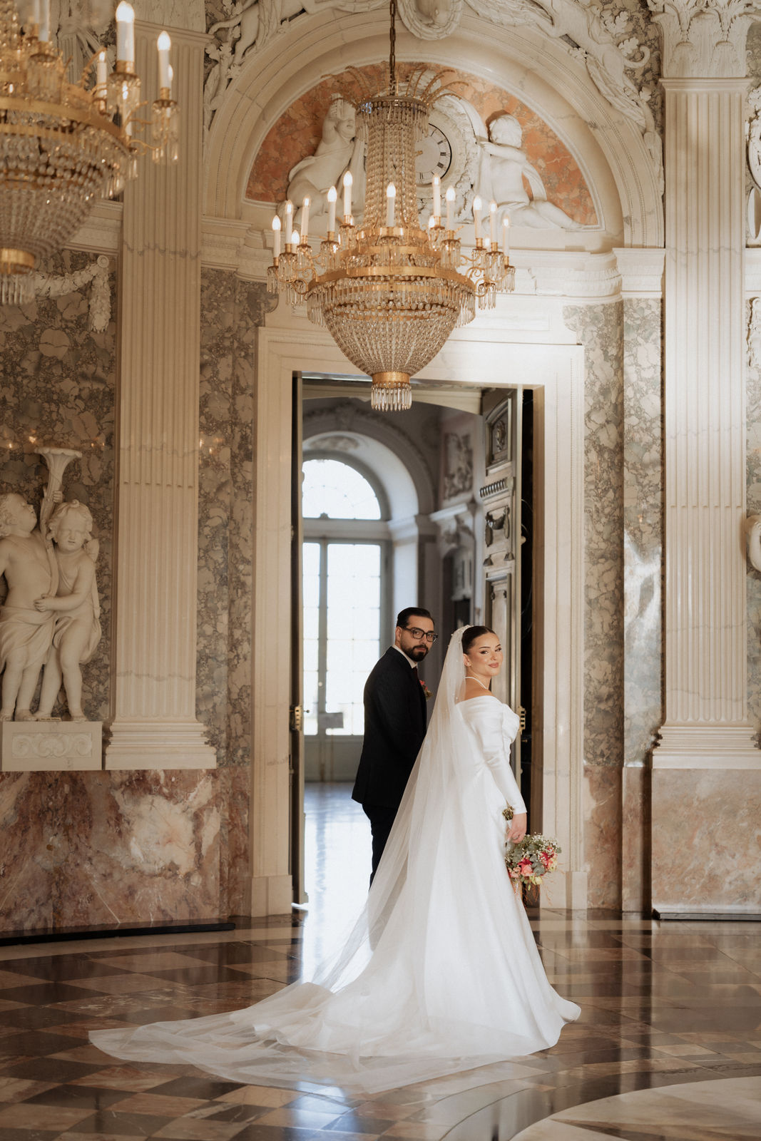 Brautpaar im prunkvollen Saal von Schloss Benrath in Düsseldorf unter dem Kronleuchter.