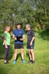 Ein Trainer mit Klemmbrett spricht mit einem Mann und einer Frau auf einer Wiese.