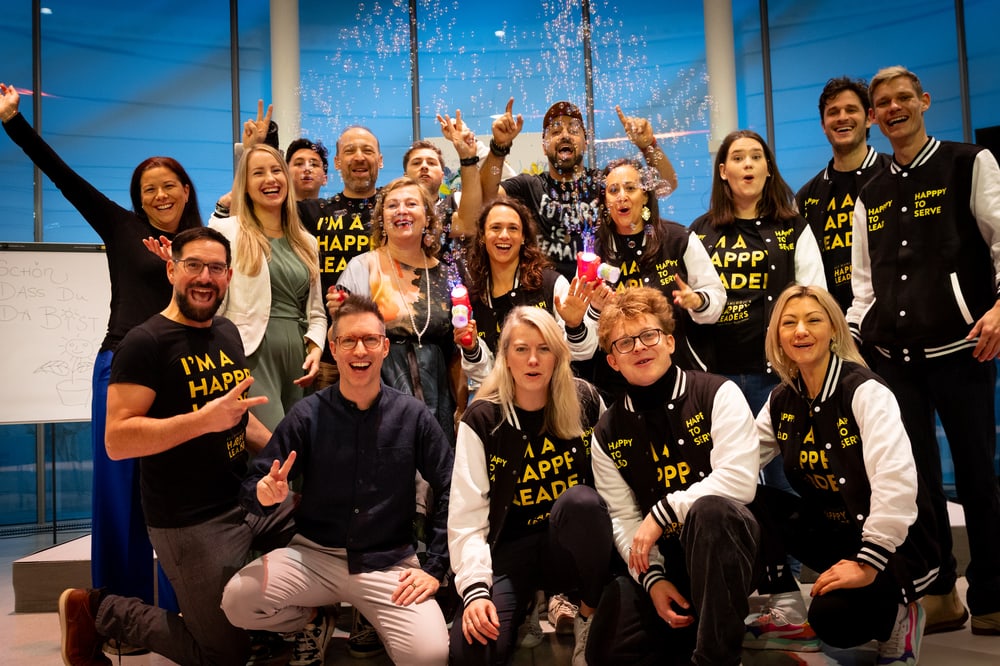 Ali Mahlodji mit dem futureOne-Team in schwarzen „Happpy Leader“-Jacken, jubelnd unter Seifenblasen