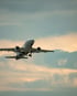 Weißes Flugzeug mit ausgefahrenem Fahrwerk hebt vor einem bewölkten Himmel ab.