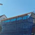 Gebäude mit Gerüst, blauen Schutznetzen und sichtbarem Holzdachstuhl unter klarem blauem Himmel.