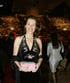 A woman in a black halter dress with pink floral embroidery holds a pink clutch, smiling in a large venue.