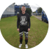 Mann in schwarzem Hoodie mit "Route 66" und schwarzer Hose mit roten Mustern steht auf Gras vor Subaru-Autohaus.
