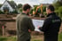Zwei Männer betrachten einen Bauplan auf einer Baustelle mit Bagger und Erdaushub für den Garten- und Landschaftsbau.