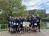 Eine Gruppe von 16 Läufern in blauen T-Shirts posiert für ein Gruppenfoto; eine Person hält ein „LETS GO reanmo!“-Schild.