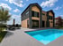 Modernes Einfamilienhaus mit Pool, Terrasse, Loungemöbeln und Garten unter blauem Himmel.