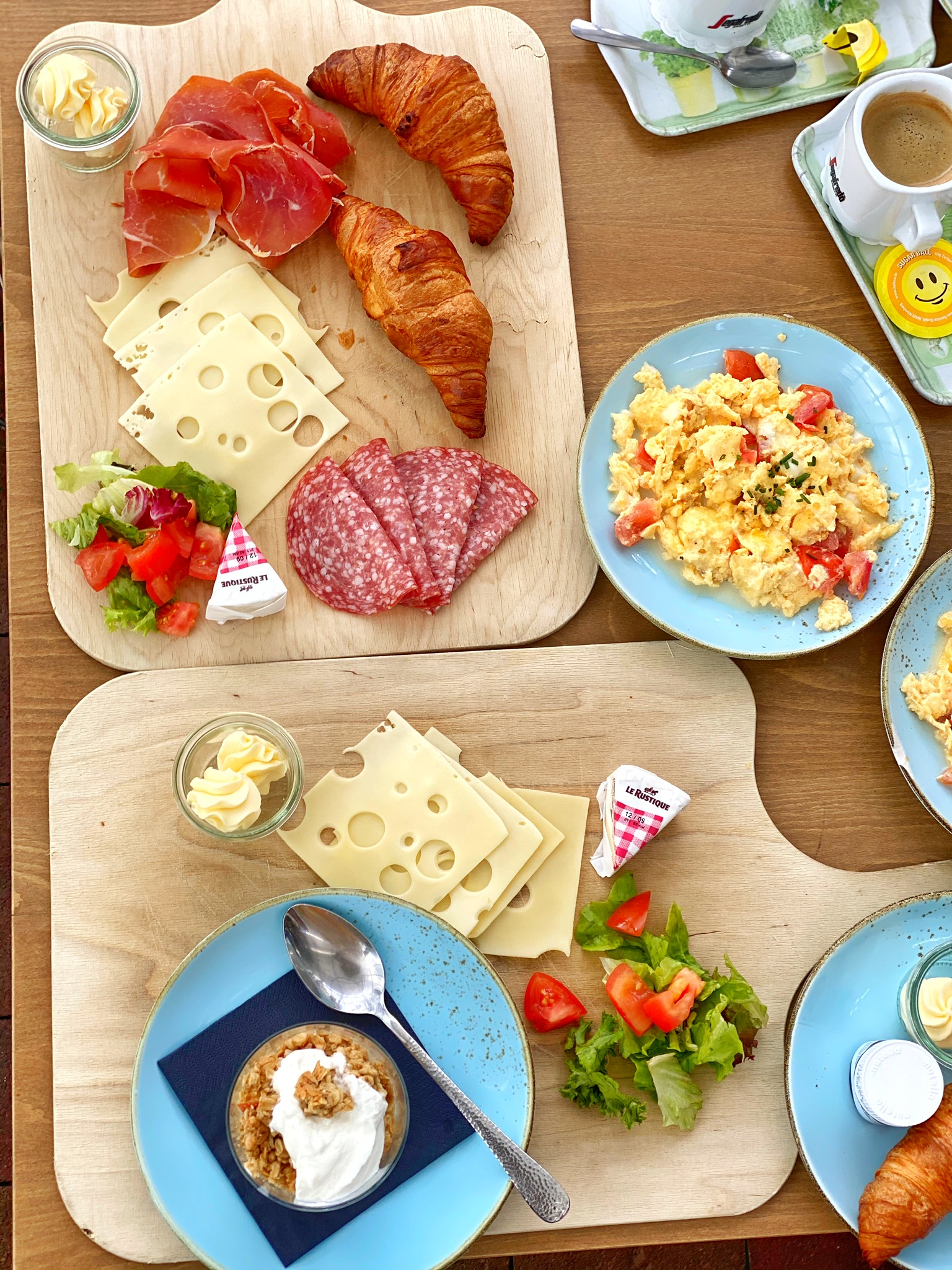 Gedeckter Frühstückstisch mit Rührei, Käse, Salami, Croissant und Erdbeeren
