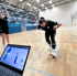 Sportlerin in einer Sporthalle bei einer Biomechanik-Analyse mit Sensoren am Bein und Laptop-Anzeige der Fußdruckmessung.
