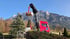 Roter LKW mit Kranarm hält eine Holzpalette vor einem Bergpanorama.