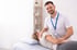 Physiotherapeut in weißem Poloshirt massiert den Nacken einer Patientin, die auf einer Liege liegt.