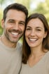 Ein Mann und eine Frau lächeln mit perfekten Zähnen in die Kamera.