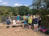 Eine Gruppe von Wanderern macht Rast an Holzbänken neben einer Brücke in einer bewaldeten Hügellandschaft.