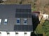 Solarmodule auf einem dunklen Ziegeldach eines weißen Hauses mit Dachfenstern.