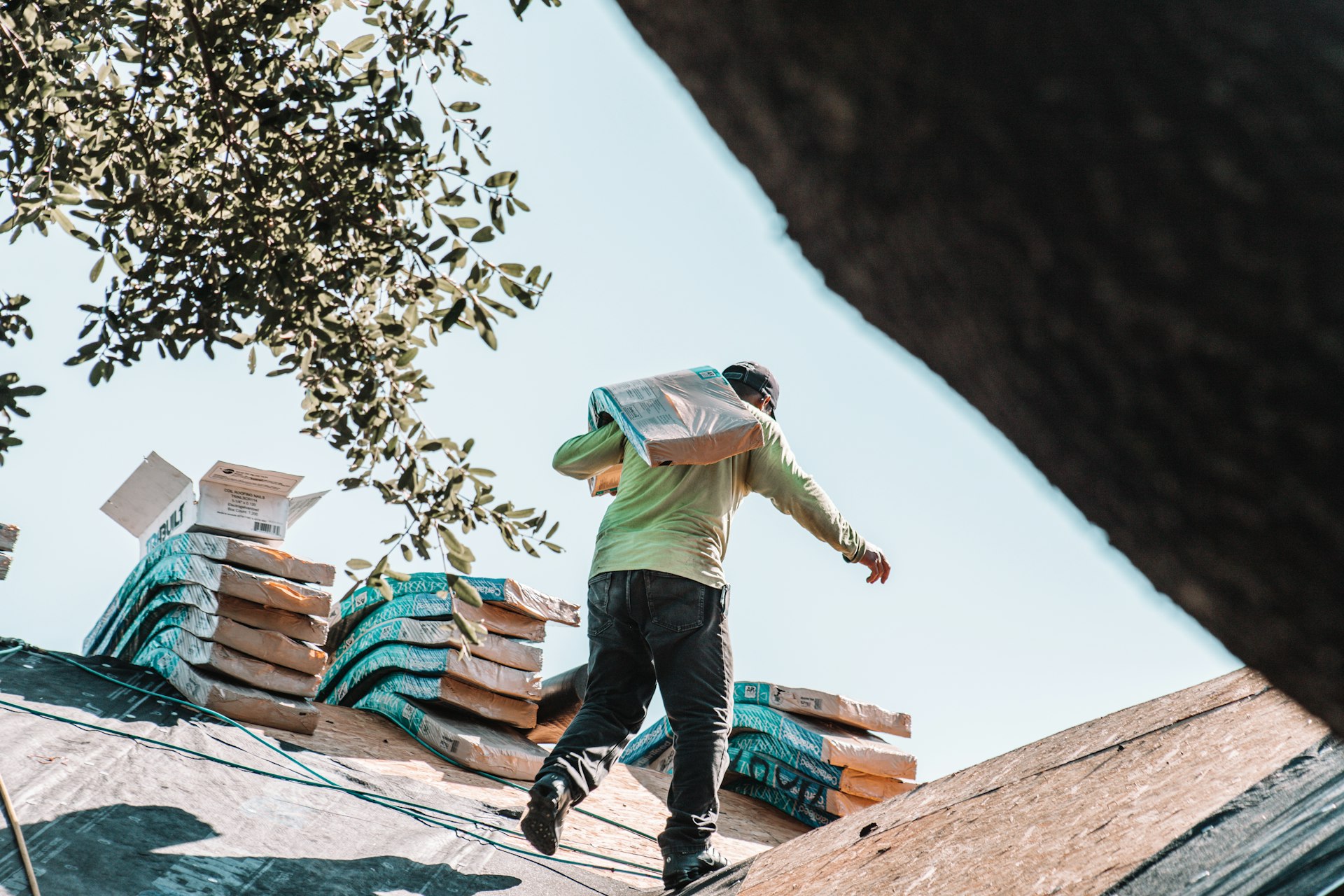 Roofer carrying a bundle of shingles across a roof during a re-roof that needs a Plano roofing permit
