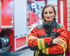 Feuerwehrfrau mit verschränkten Armen vor einem roten Feuerwehrauto.