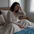 A woman sits in bed rubbing her eyes next to a digital alarm clock displaying 4:30.