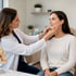 Female doctor examining a woman's jawline and chin in a medical office.