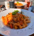 Ein Teller Fusilli-Pasta mit Tomatensoße, Gemüse und Basilikumblättern, bestreut mit Parmesan.