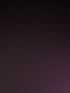Froschperspektive eines modernen Gebäudes bei Nacht mit einer Glasfassade, die in Violett, Pink und Blau beleuchtet ist.