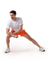 Ein Mann in einem weißen T-Shirt und orangefarbenen Shorts dehnt sich mit einem seitlichen Ausfallschritt.