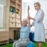 A therapist assists an elderly woman with arm exercises.