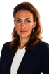 Eine Frau mit braunen Haaren, blauen Augen und pinkem Lippenstift trägt einen dunkelblauen Blazer und ein weißes T-Shirt.