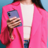 Frau in pinkem Blazer und weißem Top hält lila Smartphone.